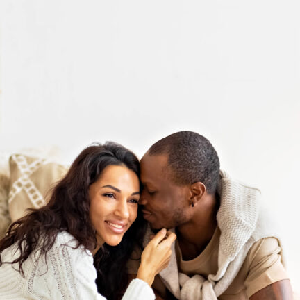 A couple in love - a black man and a mulatto woman on a bed in a bright room. Diverse family.