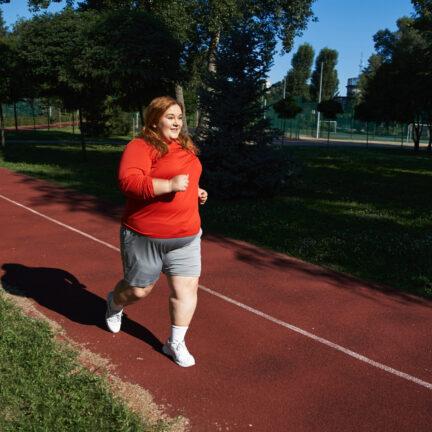 A joyful woman runs on a track, enjoying her workout in the warm sunlight.